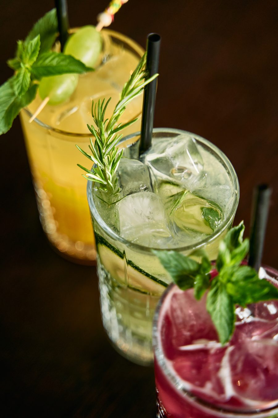 Three garnished cocktails on a dark bar top